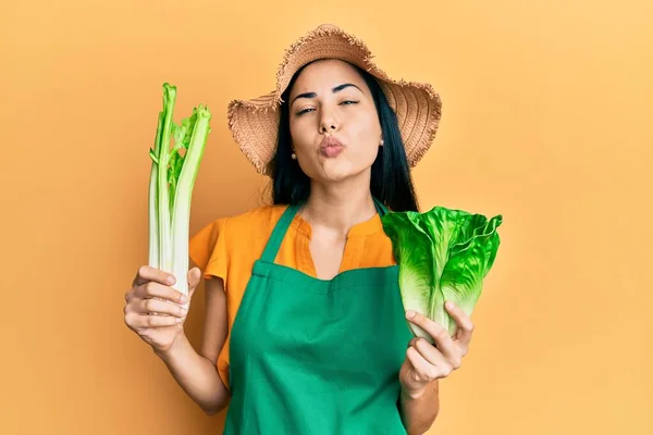 美しい若い女性が庭師のエプロンを着て カメラを見て野菜を保持します 愛の表現 — ストック写真