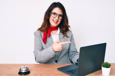 Otel resepsiyonunda çalışan genç, güzel esmer kadın dizüstü bilgisayar kullanarak mutlu bir şekilde elini ve parmağını gösterdi. 