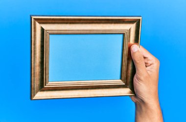 İzole edilmiş mavi arka planda eski bir çerçeveyi tutan İspanyol bir adamın eli..