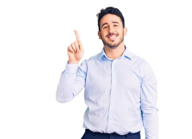 Genç İspanyol adam iş kıyafetleri giyip bir numarayı gösterip işaret ederken kendinden emin ve mutlu bir şekilde gülümsüyor.. 