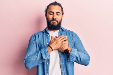 Gündelik kıyafetler giyen genç Arap adam elleri göğsünde gülümsüyor, gözleri kapalı ve yüzünde minnet ifadesi var. sağlık kavramı. 