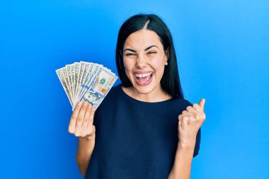 Dolarları tutan çok mutlu ve heyecanlı genç bir kadın kollarını kaldırmış, gülümseyen ve başarı için çığlık atan kazanan bir jest yapıyor. kutlama konsepti. 