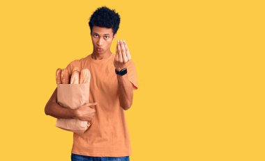 Afrika kökenli Amerikalı genç bir adam elinde bir torba ekmek tutarak italyan jesti yapıyor ve parmakları kendinden emin. 