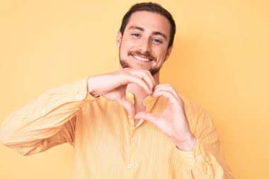 Gündelik kıyafetler giyen, aşık gülümseyen ve elleriyle kalp sembolü çizen genç yakışıklı bir adam. romantik kavram. 