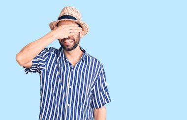 Sakallı, yaz şapkalı, çizgili gömlekli, gülümseyen ve gülen genç yakışıklı bir adam. kör kavram. 