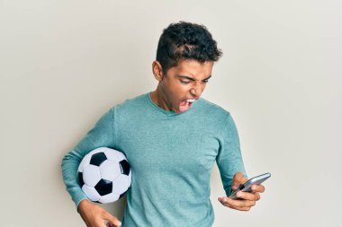 Genç, yakışıklı, Afro-Amerikan bir adam futbol topu tutuyor. Akıllı telefona bakıyor. Kızgın ve kızgın bağırıyor, öfkeyle bağırıyor. öfke ve agresif konsept. 