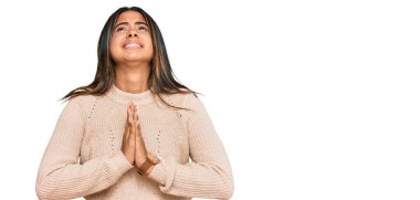 Kışlık yün kazak giyen genç Latin kız elleri bağlı yalvarıyor ve dua ediyor. Yüzünde umut ifadesi var. Çok duygusal ve endişeli. Yalvarıyor. 