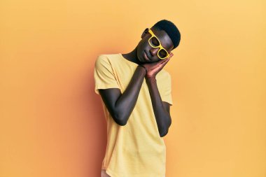 Genç Afro-Amerikalı adam günlük kıyafetler ve gözlükler takmış uyur, yorgun düşler kurar ve elleri ile poz verir, gözleri kapalı gülümserdi.. 