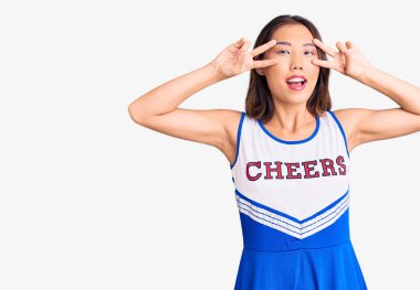 Genç, güzel Çinli kız amigo üniforması giyiyor. Barış sembolü yapıyor. Yüzünde parmaklar, gülümseyerek zaferi gösteriyor. 