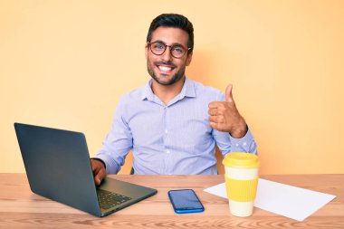 Genç İspanyol bir adam ofiste çalışıyor. Bir fincan kahve içiyor. Mutlu ve pozitif gülümsüyor. 