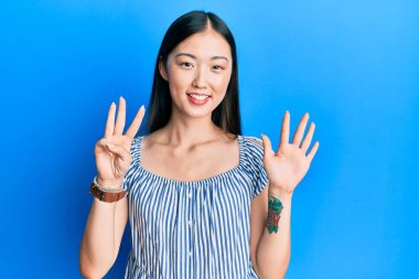 Gündelik çizgili tişört giyen Çinli genç bir kadın 8 numaralı parmaklarıyla onu gösterirken kendinden emin ve mutlu bir şekilde gülümsüyor.. 