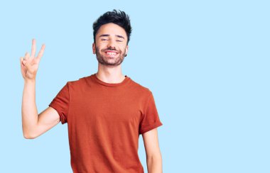 Gündelik kıyafetler giyen, gülümseyen ve kameraya göz kırpan genç İspanyol adam zafer işareti yapıyor. İki numara.. 