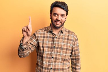 Bir fikir veya soruyla gülümseyen gündelik kıyafetler giyen genç İspanyol adam, bir numara, mutlu bir yüzle işaret ediyor. 