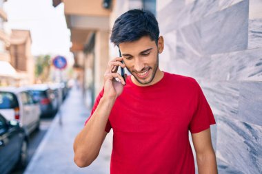 Genç Latin adam gülümsüyor ve şehirde akıllı telefondan konuşuyor..
