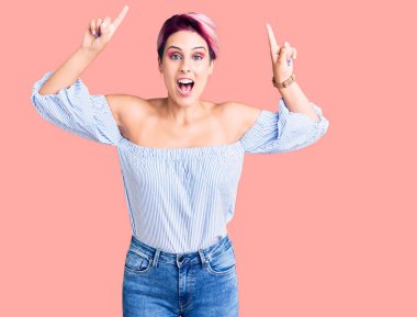 Pembe elbiseli genç bir kadın. Gülümsüyor, şaşırıyor, parmaklarıyla işaret ediyor ve kollarını kaldırıyordu.. 