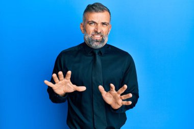 Orta yaşlı, iş gömleği giyen ve kravat takan yakışıklı bir adam. Tiksinti tepkisi yüzünden tiksinmiş ve ürkek bir ifade takınıyor. Eller havada. 