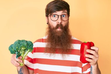 Uzun sakallı, elinde brokoli ve kırmızı biber olan yakışıklı genç kızıl saçlı adam balık suratlı ve şaşı gözlü, çılgın ve komik.. 