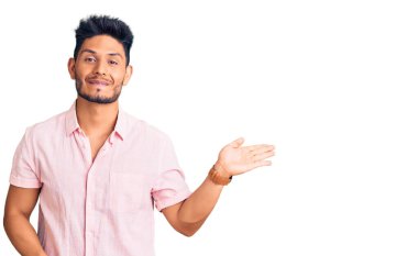 Yakışıklı Latin Amerikalı rahat bir yaz gömleği giymiş neşeli bir şekilde gülümseyen ve avuç içi kameraya bakan genç adam.. 