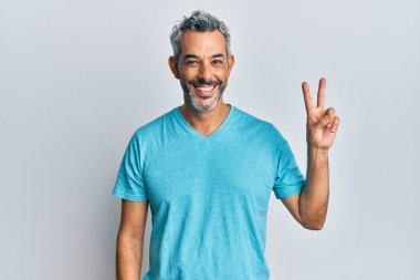 Orta yaşlı, gri saçlı, günlük kıyafetler giyen, iki numaralı parmaklarıyla işaret eden, kendinden emin ve mutlu bir adam.. 