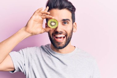 Genç, sakallı, gözünün üzerinde kivi tutan yakışıklı bir adam. Olumlu ve mutlu görünüyor. Kendine güvenen bir gülümsemeyle, dişlerini gösteriyor. 