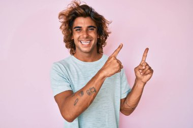 Gündelik kıyafetler giyen genç İspanyol adam gülümseyip kameraya bakıyor ve iki eliyle ve parmaklarıyla kenarı işaret ediyor.. 