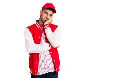 Beyzbol forması giyen genç İspanyol adam çapraz kollarla depresyon sorunlarından yorgun ve sıkılmış göründüğünü düşünüyor.. 