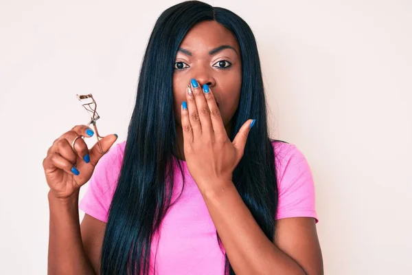 Joven Mujer Afroamericana Sosteniendo Rizador Pestañas Cubriendo Boca Con Mano —  Fotos de Stock