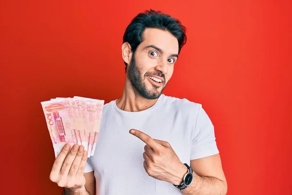 Joven Hispano Sosteniendo Billetes Chinos Yuan Sonriendo Feliz Señalando Con —  Fotos de Stock