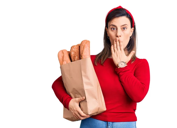 若い美しい女性の手で口をカバーパンと紙の袋を保持し ショックを受け ミスを恐れている 驚きの表情 — ストック写真