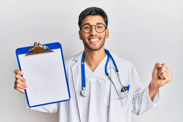 Joven Hombre Guapo Con Estetoscopio Médico Sosteniendo Portapapeles Gritando Orgulloso — Foto de Stock