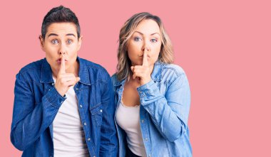 Gündelik giysiler giyen ve parmakları dudaklarında sessiz olmak isteyen iki kadın. sessizlik ve gizli konsept. 