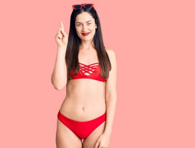 Bikini giyen güzel beyaz bir kadın bir numarayı gösterip işaret ederken kendinden emin ve mutlu bir şekilde gülümsüyor.. 