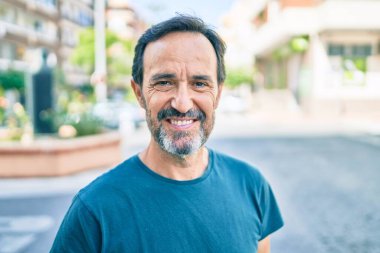 Orta yaşlı, sakallı, açık havada mutlu gülümseyen bir adam.