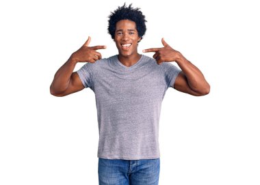 Afro saçlı, sıradan kıyafetler giyen, neşeli gülümseyen ve parmaklarıyla ve ağzıyla işaret eden yakışıklı Afro-Amerikan erkeği. diş sağlığı kavramı. 