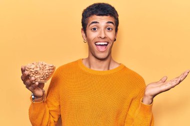 Elinde fıstıkla zaferi kutlayan genç bir Afrikalı Amerikalı adam mutlu bir gülümseme ve kaldırılmış bir el ile kazanan bir ifade. 