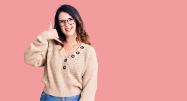 Güzel, genç, esmer, günlük kıyafetler ve gözlük takan, gülümseyen, el ve parmaklarıyla telefonla konuşan bir kadın. iletişim kavramları. 