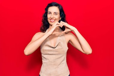 Gündelik kıyafetler giyen, aşık gülümseyen, elleriyle kalp sembolü yapan genç, güzel İspanyol bir kadın. romantik kavram. 