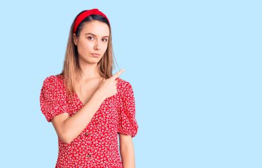 Elbise giymiş güzel bir kız ve diadem parmağıyla yan tarafı işaret ediyor. Ciddi ve sakin bir yüz ifadesi var. 