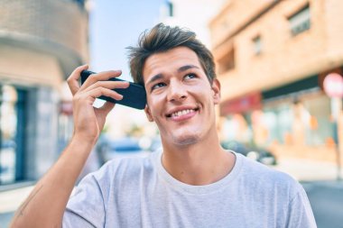 Kafkasyalı genç adam gülümsüyor. Şehirdeki akıllı telefonu kullanarak mutlu bir şekilde sesli mesaj dinliyor..