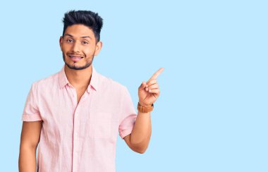 Yakışıklı Latin Amerikalı rahat bir yaz gömleği giyen yüzünde kocaman bir gülümseme olan, kameraya el ile işaret eden genç adam.. 