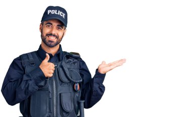 Polis üniforması giyen genç İspanyol adam avuçlarını gösteriyor ve baş parmağıyla iyi bir hareket yapıyor, mutlu ve neşeli gülümsüyor. 
