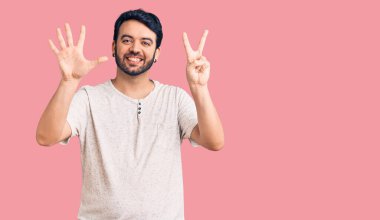 Gündelik kıyafetler giyen genç İspanyol adam yedi numarayı gösterip işaret ederken kendinden emin ve mutlu bir şekilde gülümsüyor.. 
