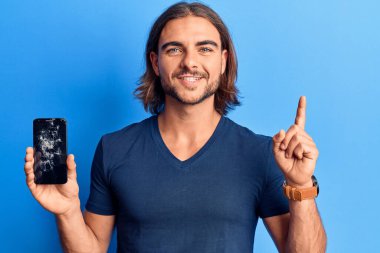 Kırık bir ekranda kırık akıllı telefon tutan genç yakışıklı bir adam bir fikir ya da soru işareti ile şaşırdı. 