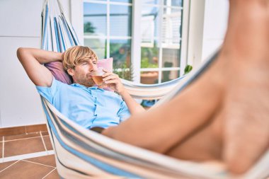 Evinin terasında orta yaşlı yakışıklı bir adam hamakta dinleniyor ve taze bira içiyor.