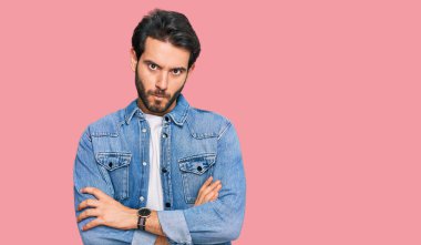 Gündelik kıyafetler giyen, kuşkucu ve gergin genç İspanyol bir adam. Yüzünde çapraz kollarla onaylamayan bir ifade var. negatif kişi. 