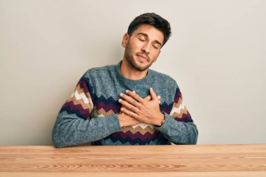 Masada oturan, elleri göğsünde, gözleri kapalı ve yüzünde minnet dolu bir jestle gülümseyen, sıradan bir süveter giyen genç yakışıklı adam. sağlık kavramı. 