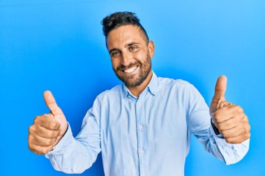 Sakallı, sıradan kıyafetler giyen, eli ile olumlu jest yapan, gülümseyen ve başarı için mutlu olan yakışıklı bir adam. kazanan jest. 