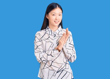 Genç, güzel, Çinli bir kadın, sıradan bir tişört giyiyor, alkışlıyor, mutlu, neşeli ve gururlu elleri alkışlıyor. 