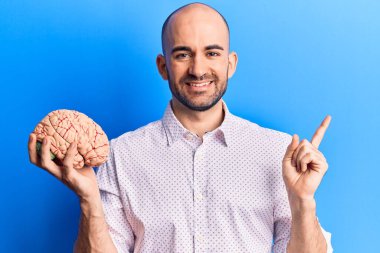 Beyni tutan yakışıklı kel adam gülümsüyor. Mutlu bir şekilde elini ve parmağını yana doğru gösteriyor. 