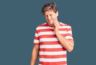 Sıradan kıyafetler giyen genç yakışıklı bir adam diş ağrısı ya da diş hastalığından dolayı acı dolu bir ifadeyle ağıza dokunuyor. dişçi 